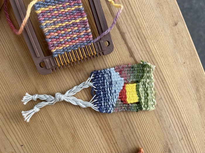 Mini arazzo con un paesaggio tessuto, appeso a un filo